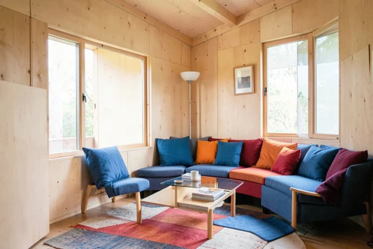 Interior de uma cabana modular com móveis simples e decoração minimalista, luz natural entrando pelas janelas.